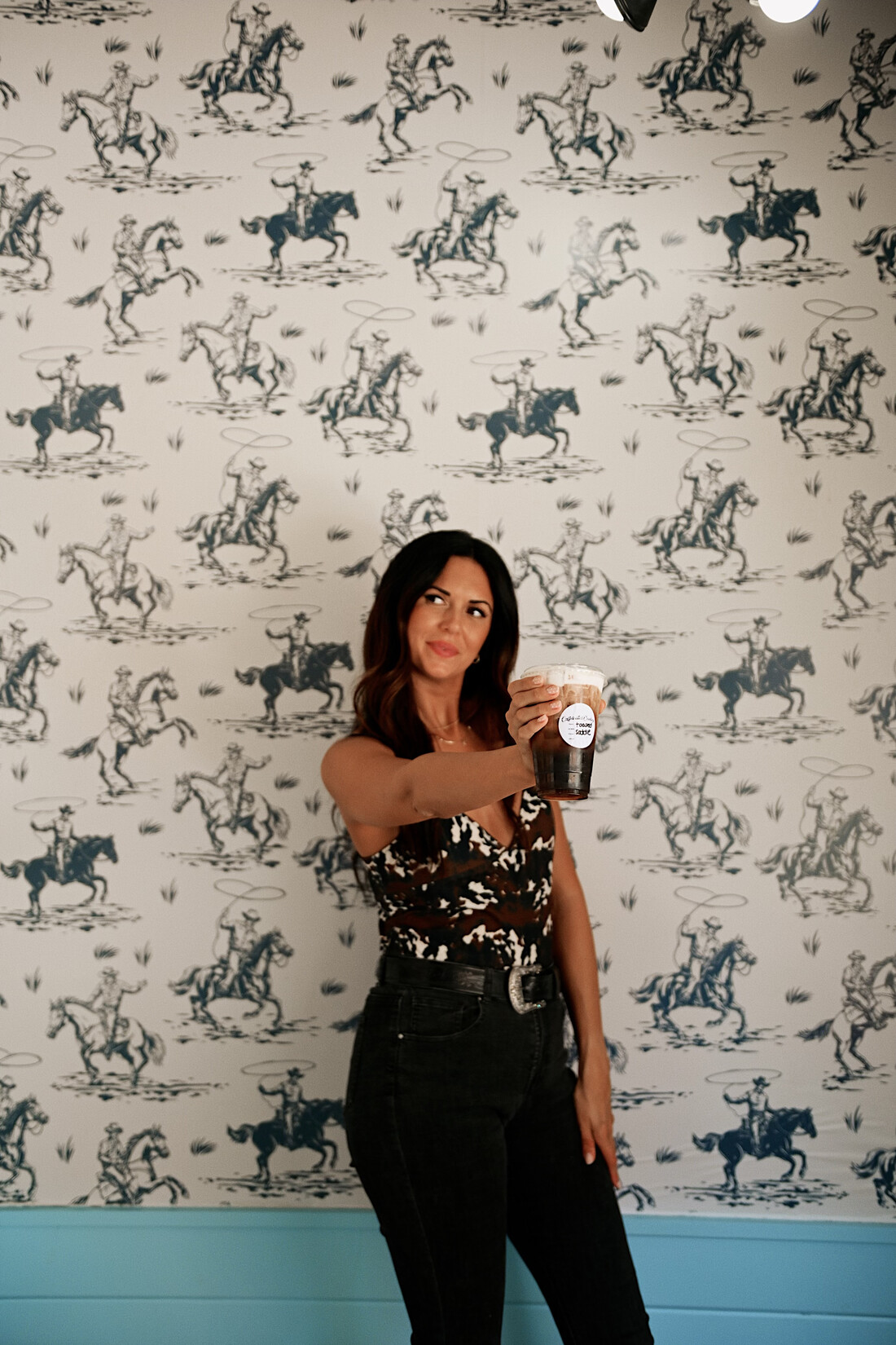 A Caffeinated Cowboy drink held against the shop's cowboy toile wallpaper